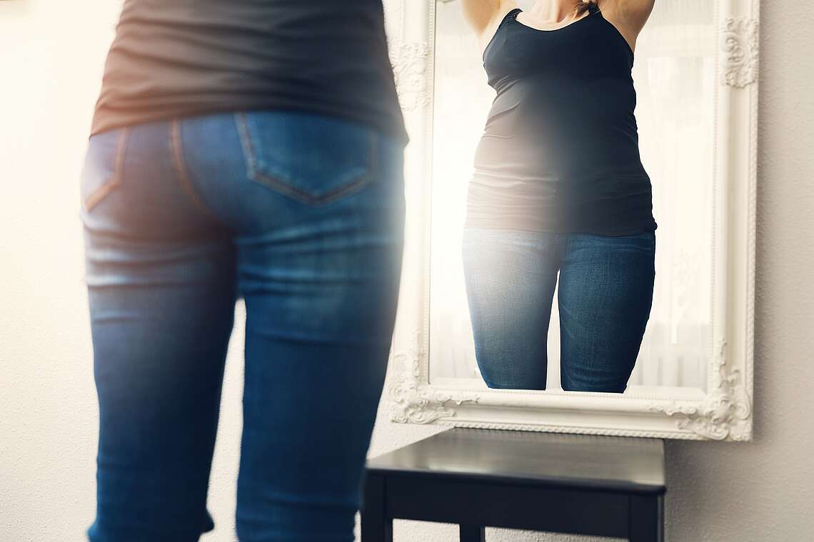 Eine Frau mit einem verzerrtem Selbstbild steht vor dem Spiegel